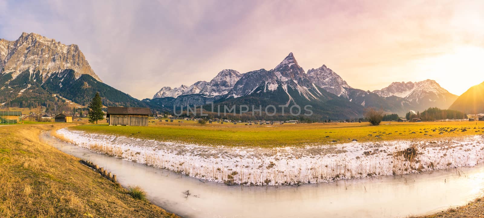Beginning of the winter  in the Austrian Alps mountains, with a frozen river, snow on the dried grass, a small village and a bright afternoon sun.