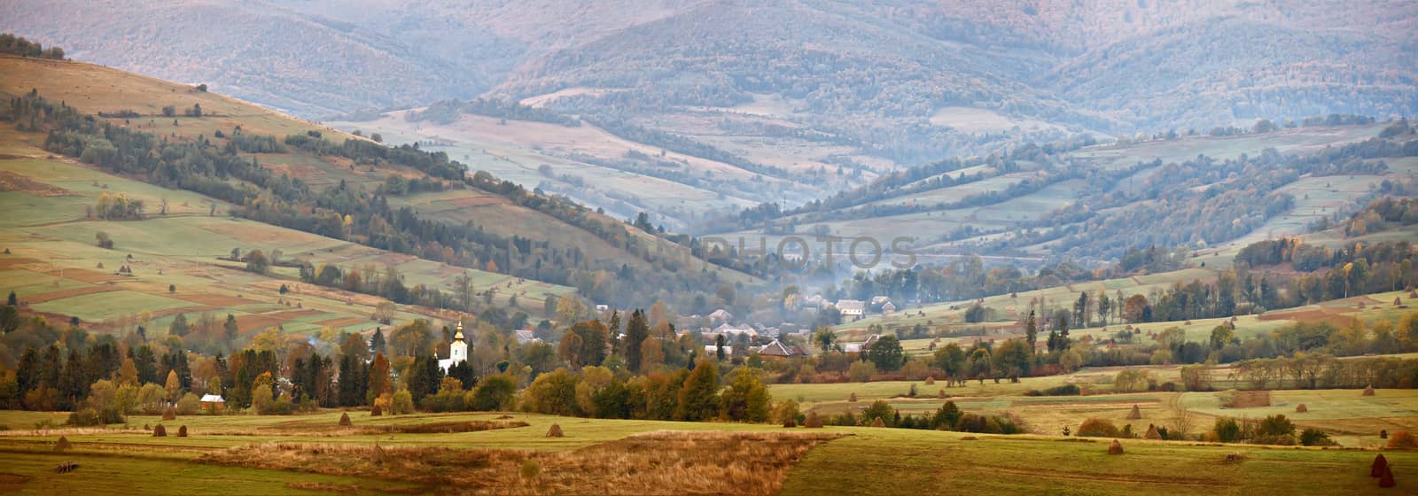 Cloudy autumn panorama in mountain hills. Village in October valley