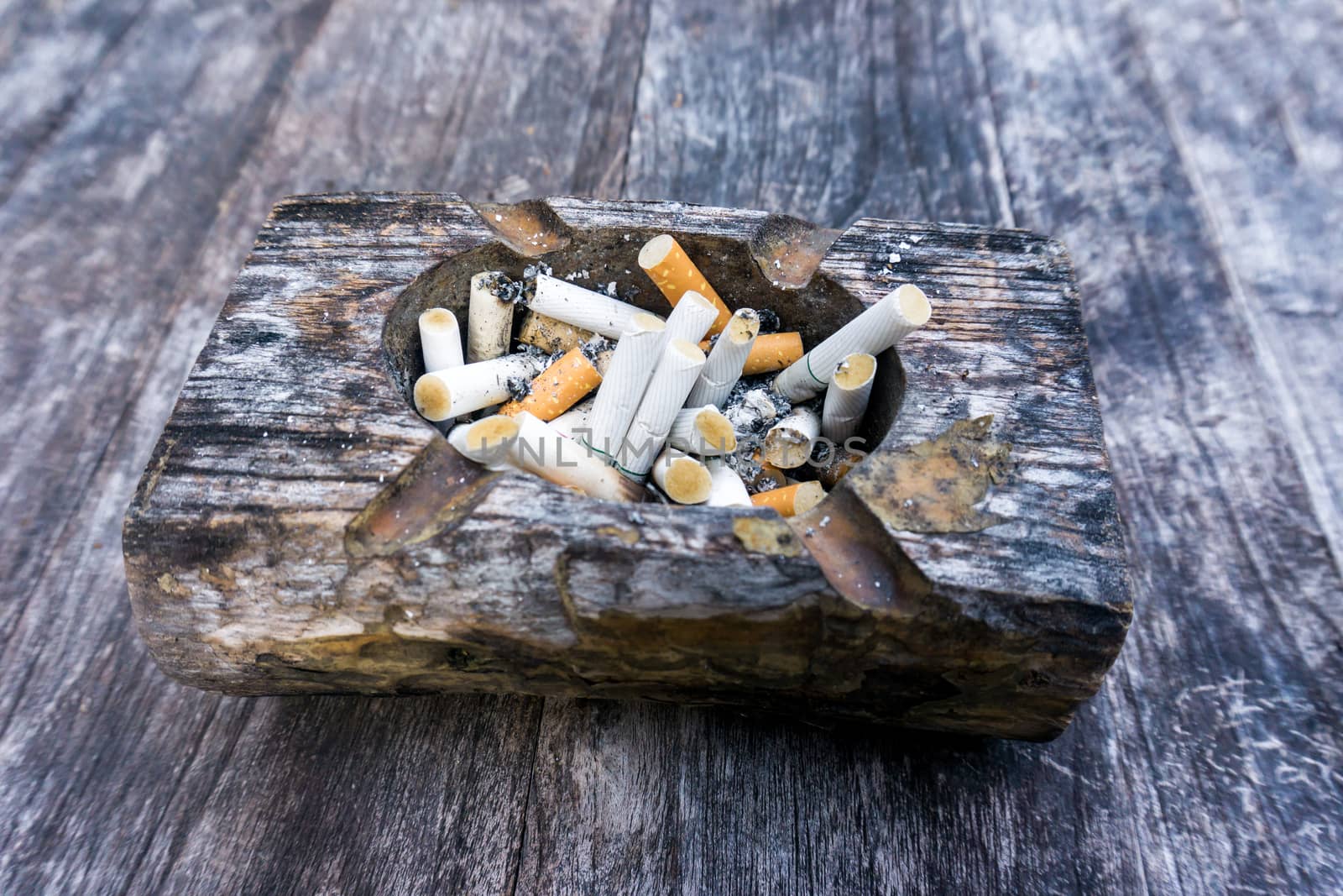 Cigarette butts with ash in ashtray on grey wooden table by nopparats