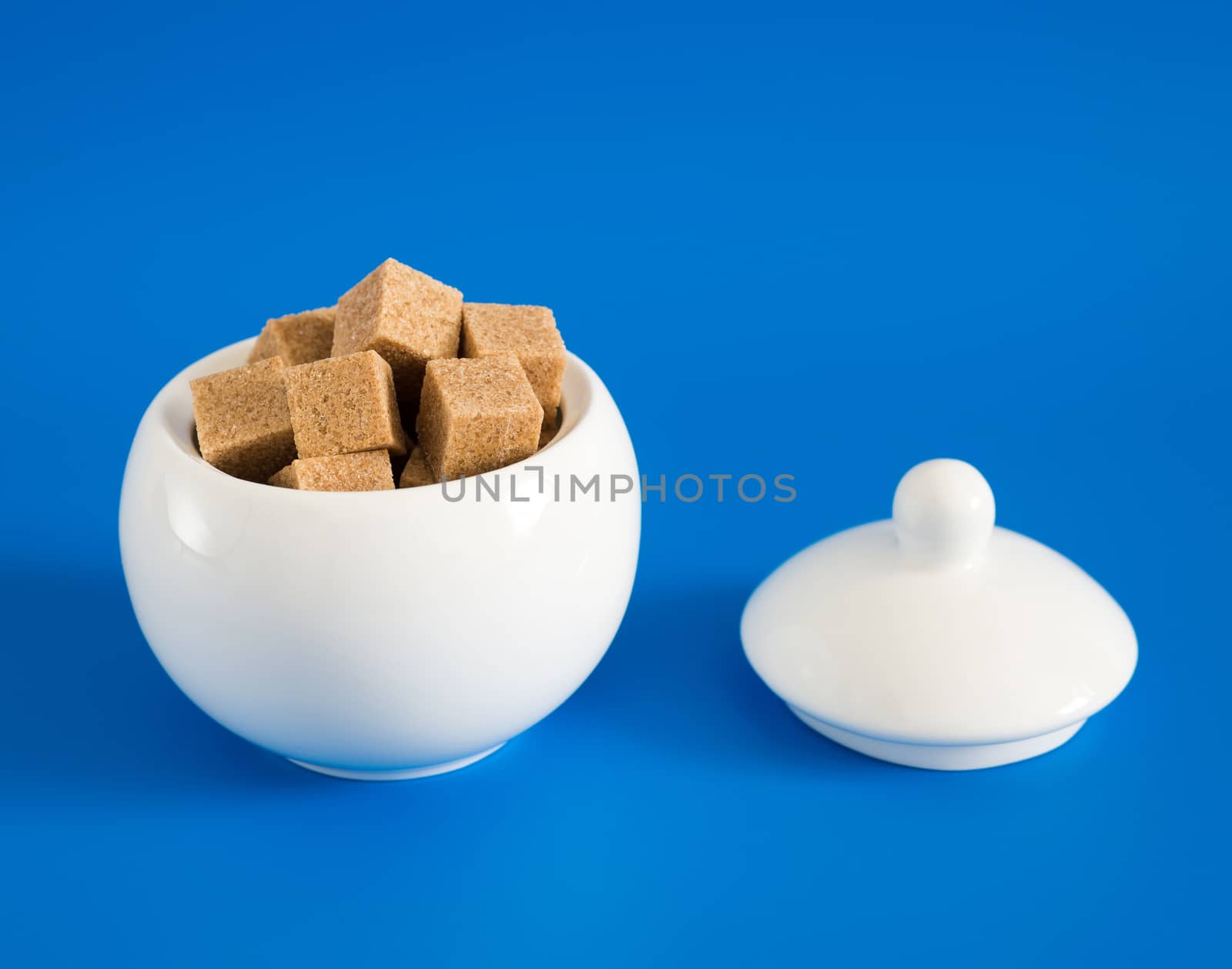 Slices of raw sugar in sugar bowl on blue background by olgavolodina