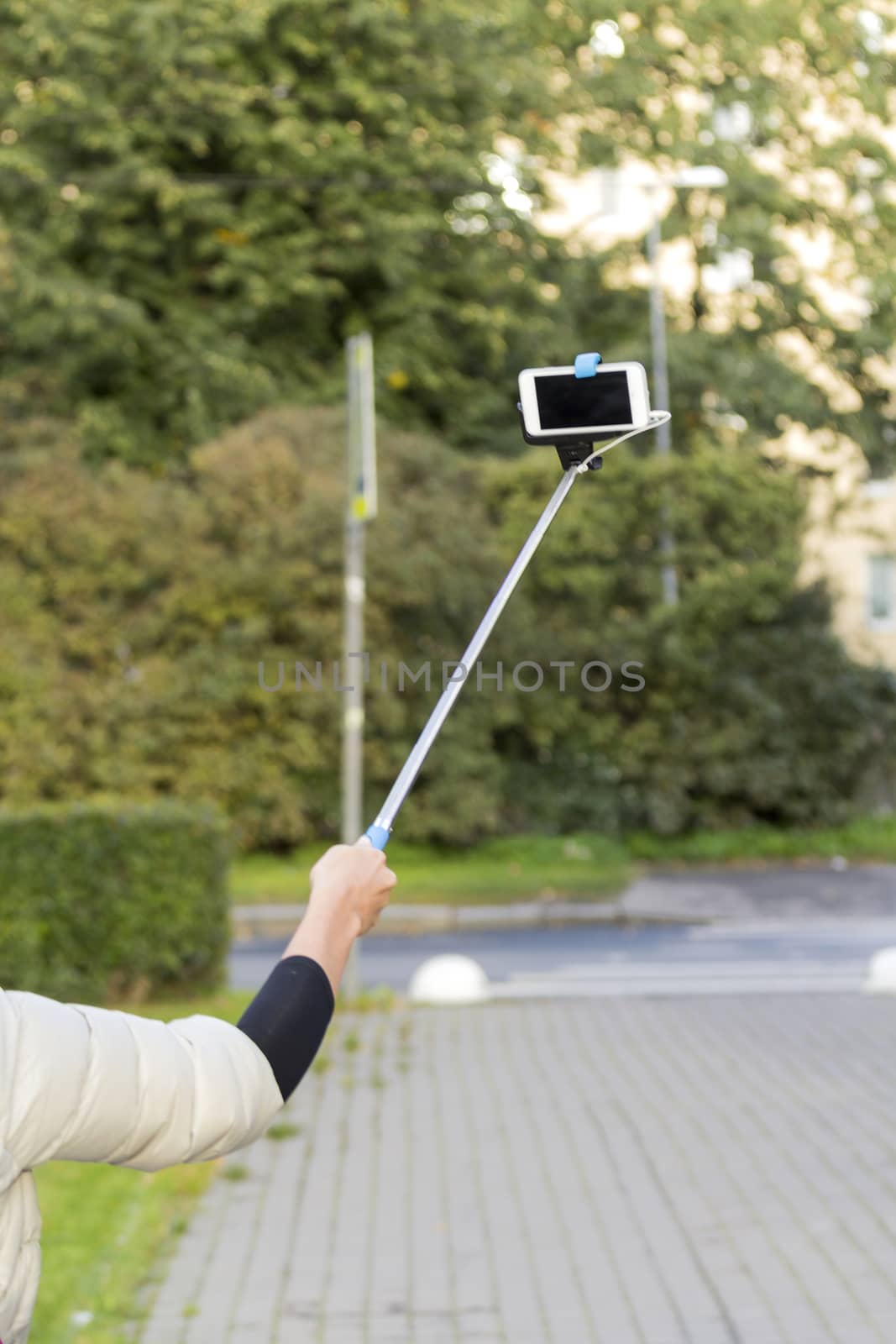The hand of a girl holding a stick with selfi Smart-phone on the road