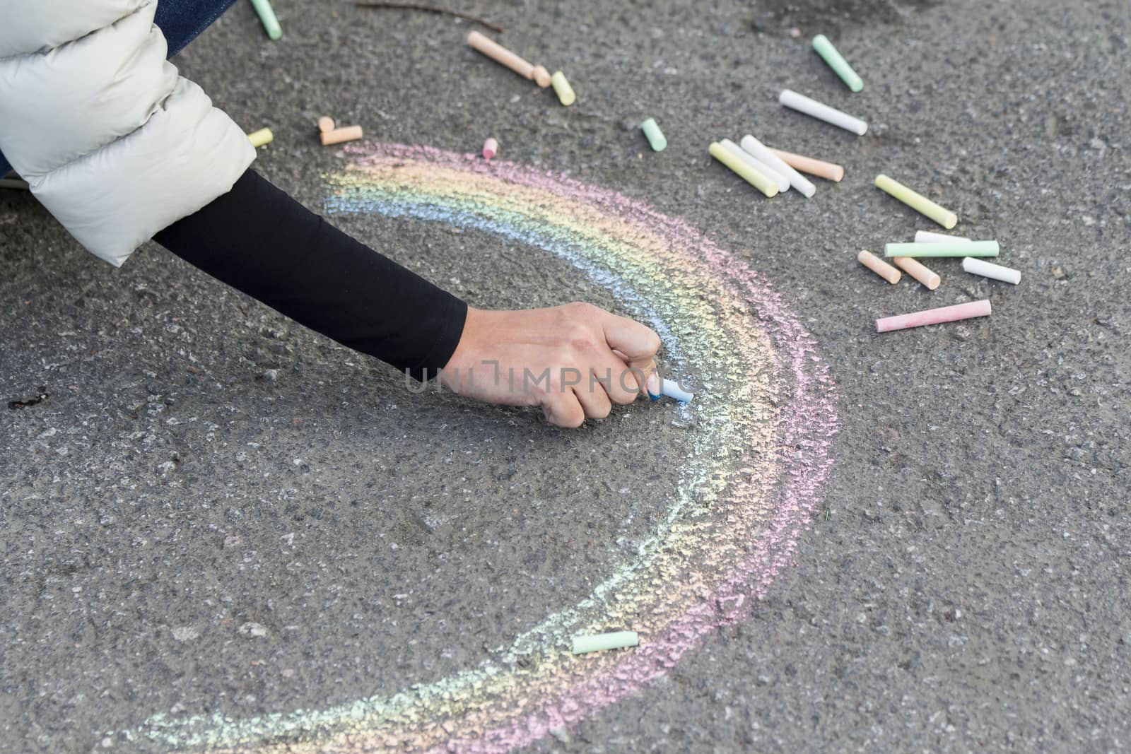 Hand draws with crayons colored Rainbow girl on the pavement