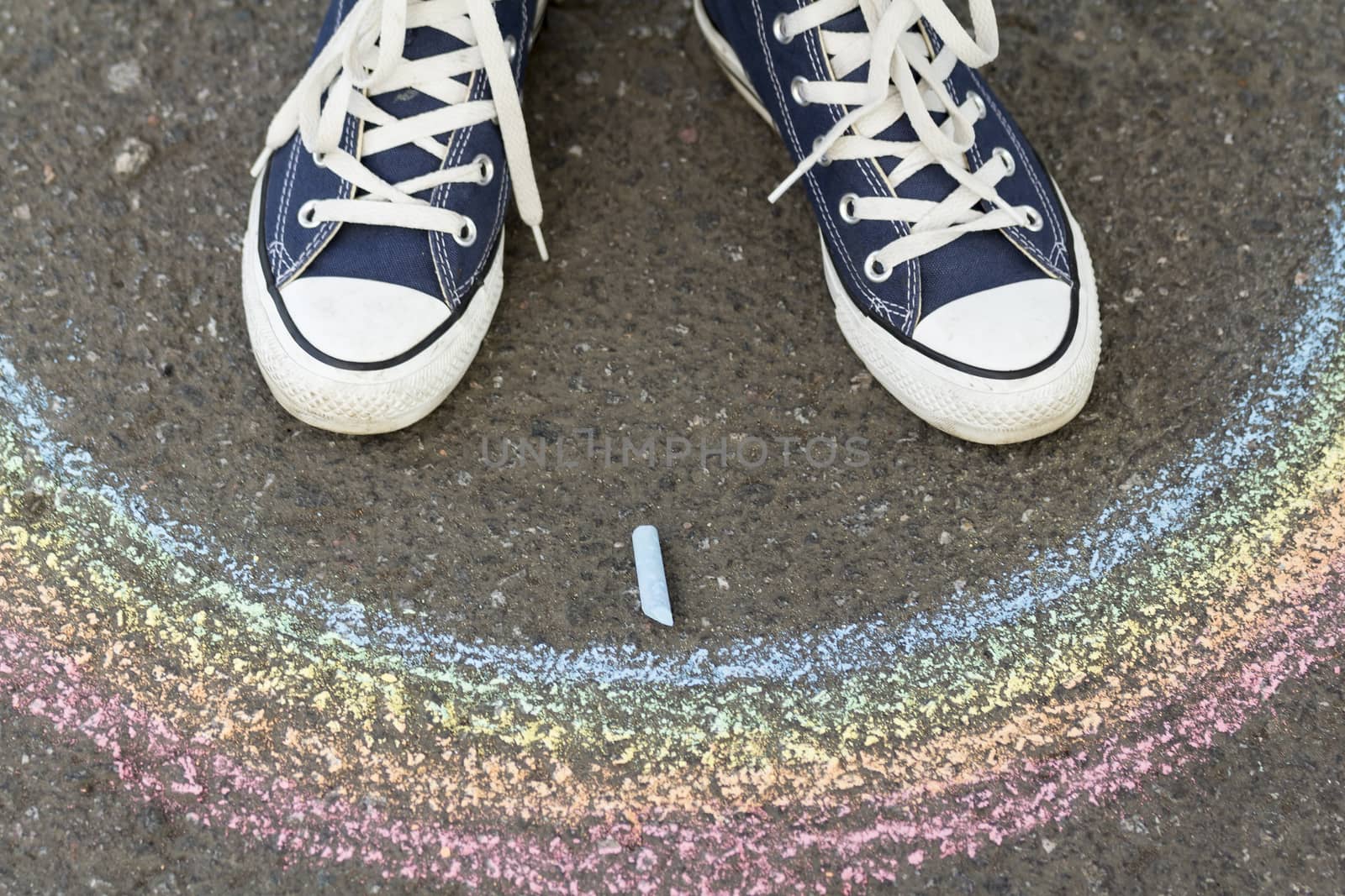 Feet in sneakers are on asphalt before drawn a rainbow