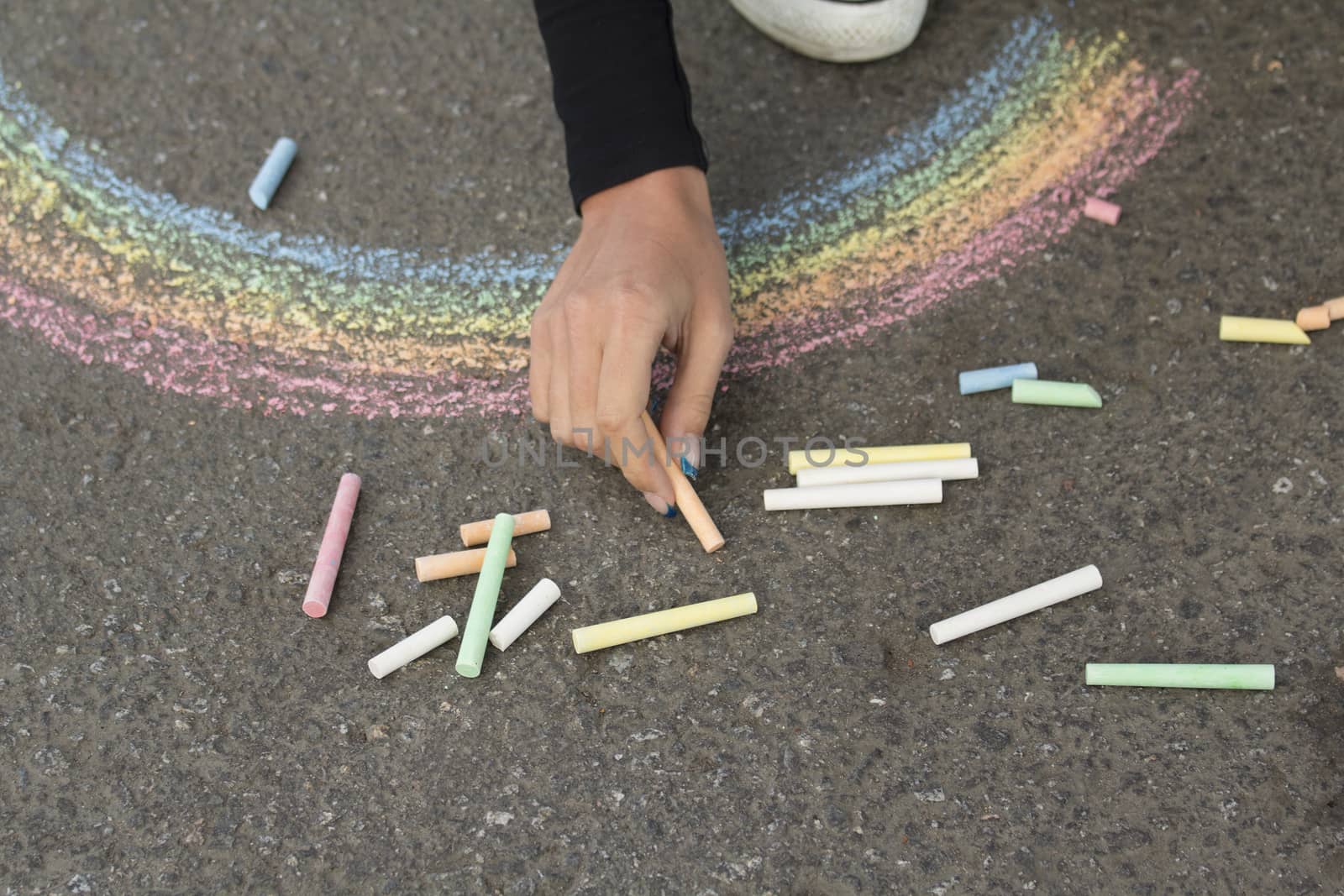 Hand draws with crayons colored Rainbow girl on the pavement