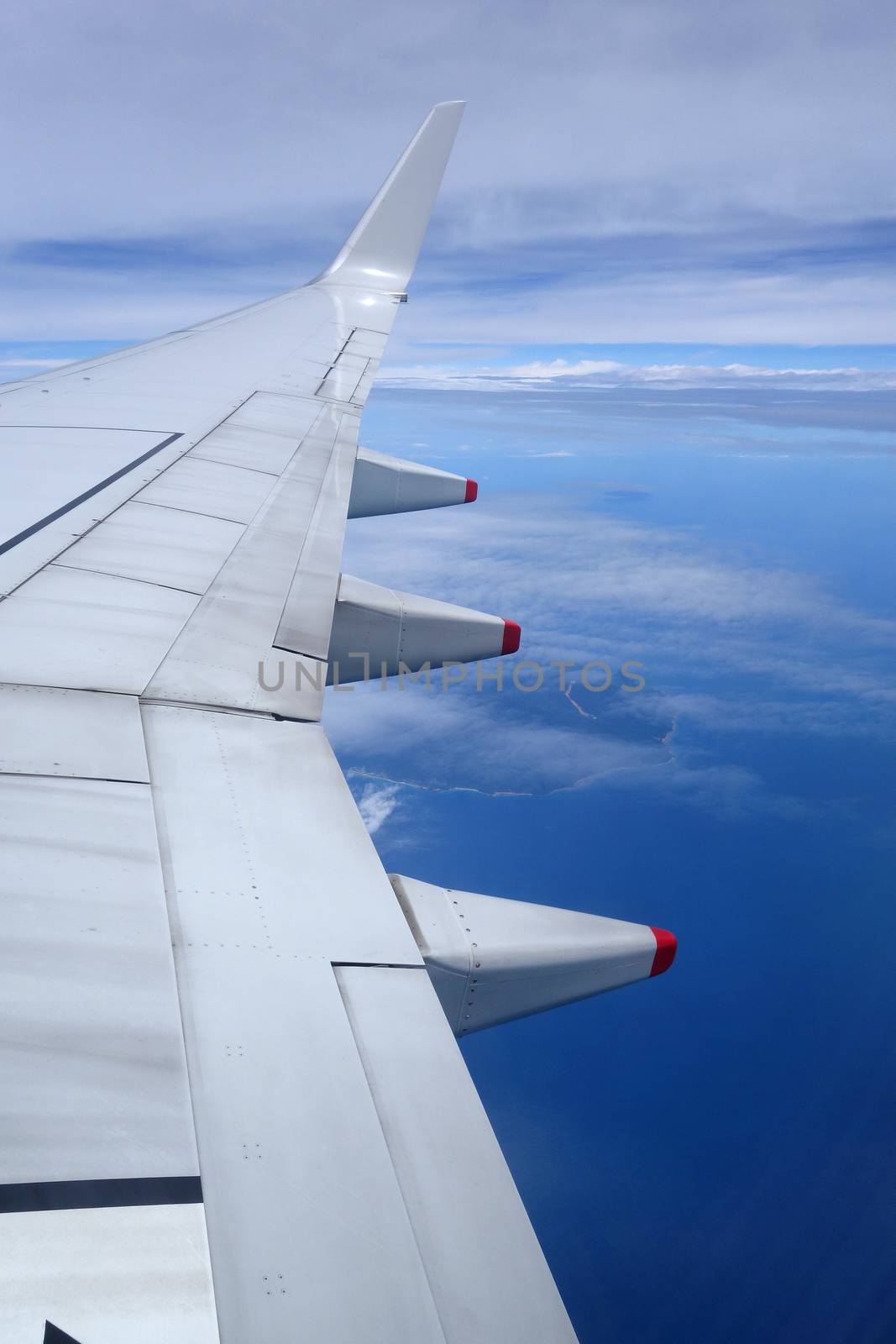 Wing of an airplane flying above the clouds on blue sky background