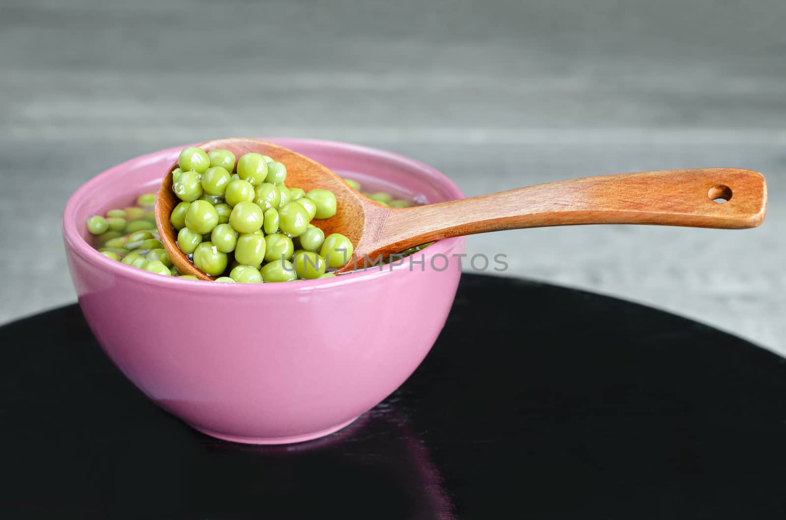 Green peas in a bowl and a wooden spoon. Old black surface and gray wooden background.