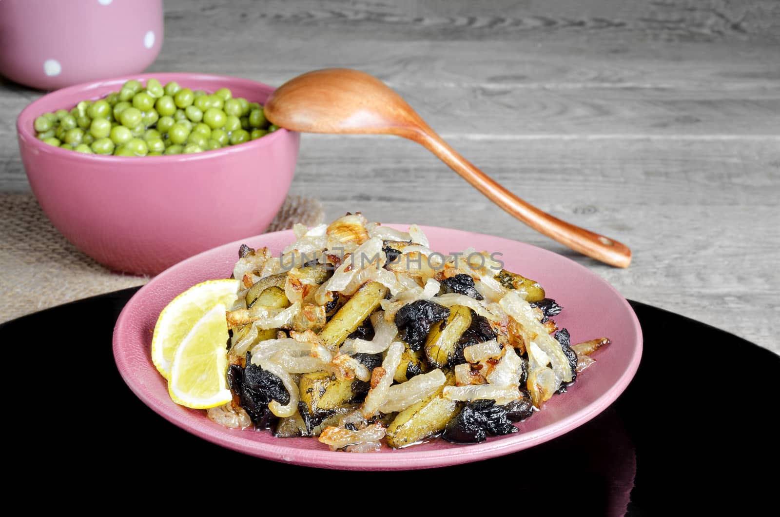 Fried potatoes with mushrooms and onions and green peas. On the black surfaces and grey wood background.