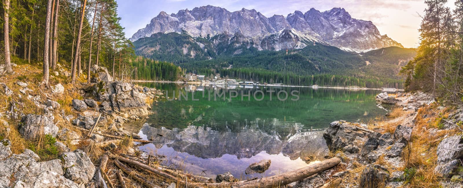 Alpine panorama with the German Alps mountains reflected in the Eibsee lake and green coniferous forest, at sunset in December.