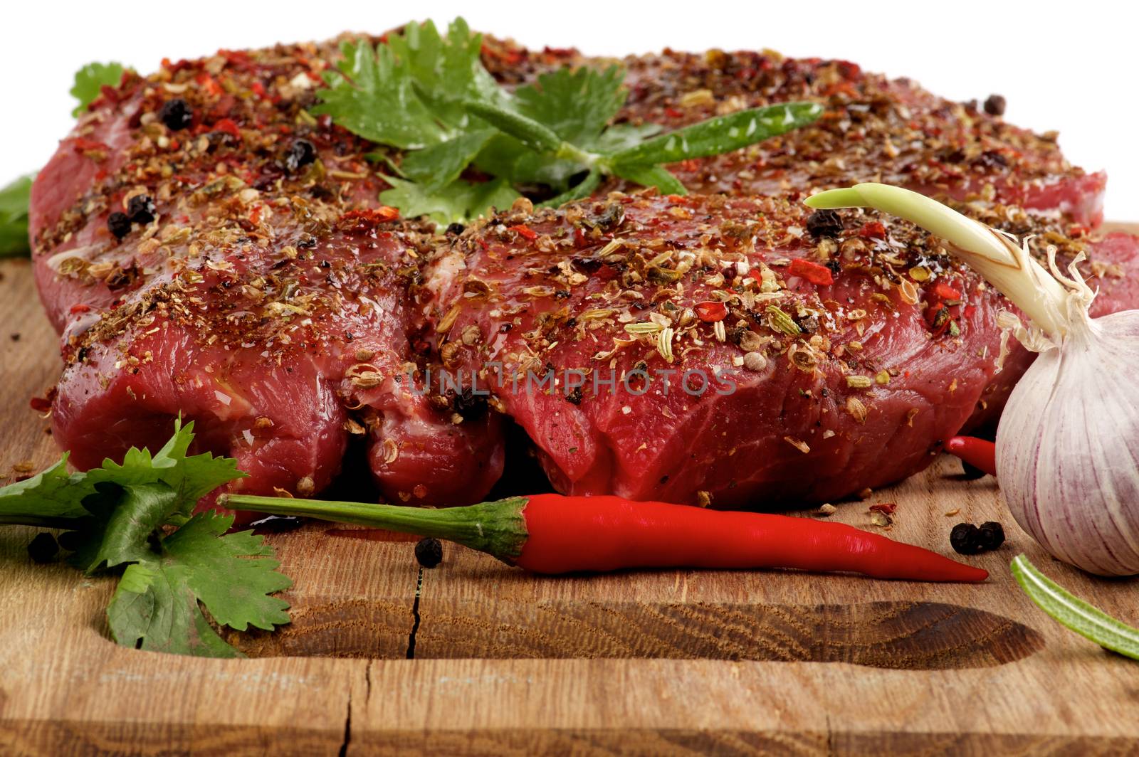 Marinated Raw Beef Steak with Herbs and Spices, Garlic and Chili Pepper closeup on Wooden Cutting Board on White background