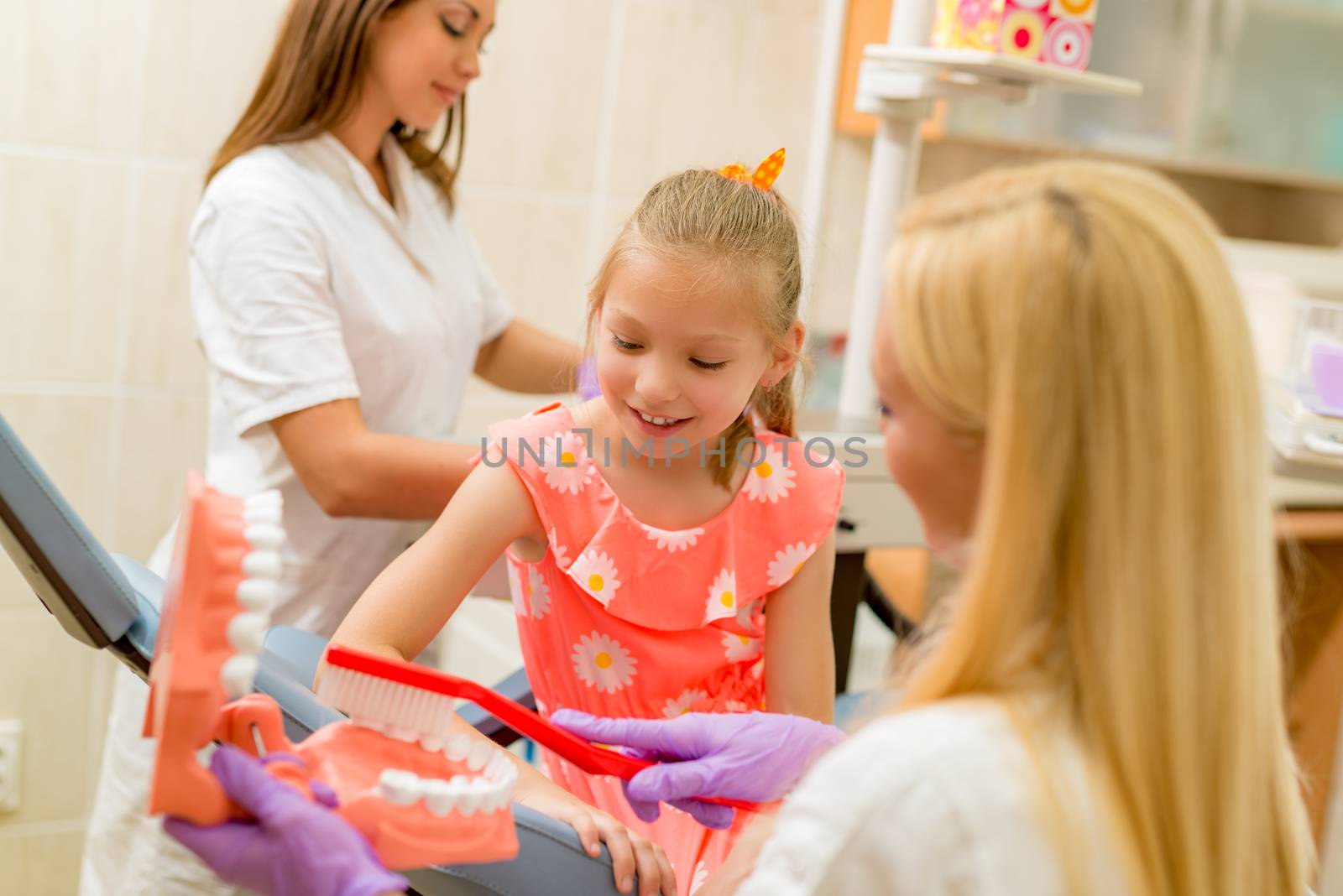 Dentist learning little girl patients how to brush her teeth with toothbrush. Selective focus. Focus on little girl.