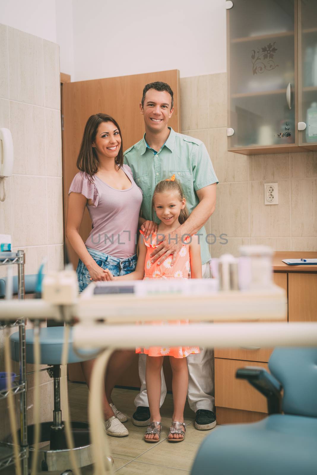 Happy young family at visit in the dentist office. They are standing and looking at camera.