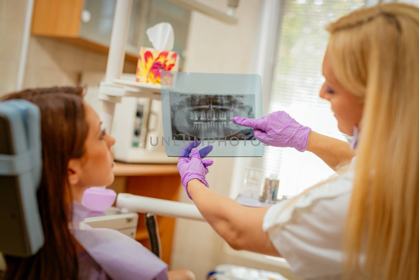 Young female dentist showing to the patient X-ray picture in she`s office. Selective focus.
