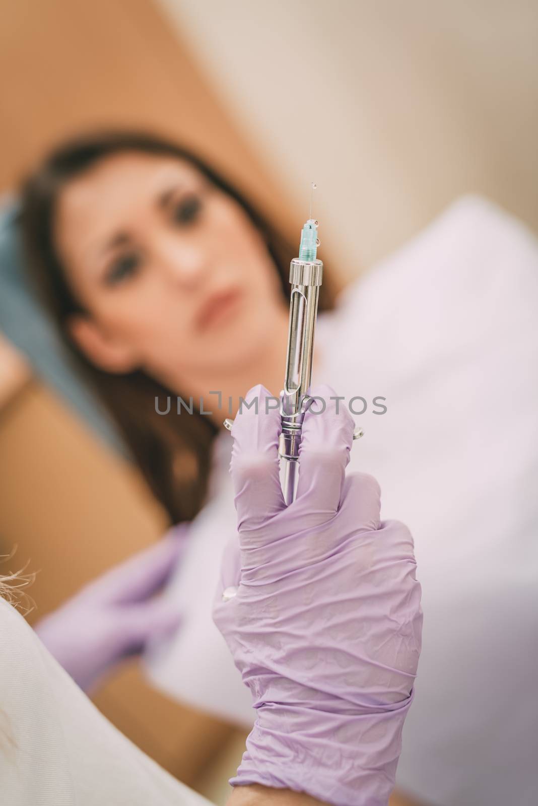 Dentist holding an injection of anesthesia. Selective focus. Focus on syringe. Female patient sitting at dental office in background.