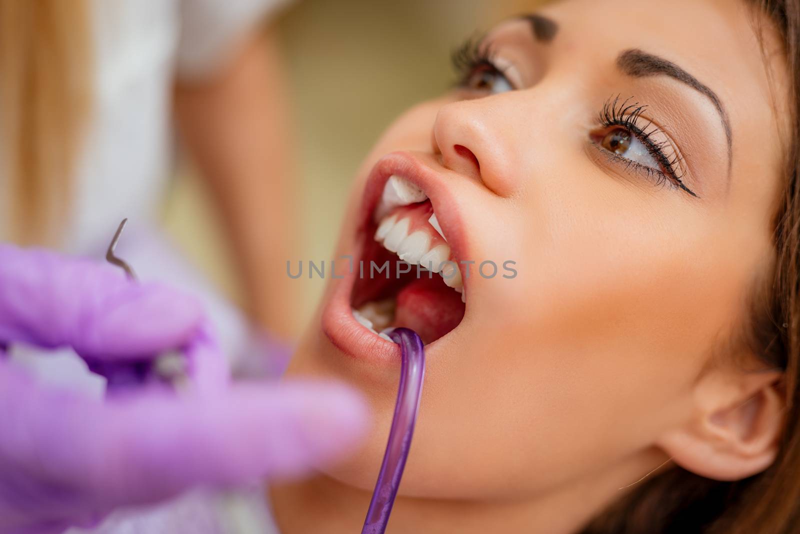 Beautiful young woman in visit at the dentist office. She is sitting on a chair and female dentist checkup teeth on her. Selective focus. Close-up.