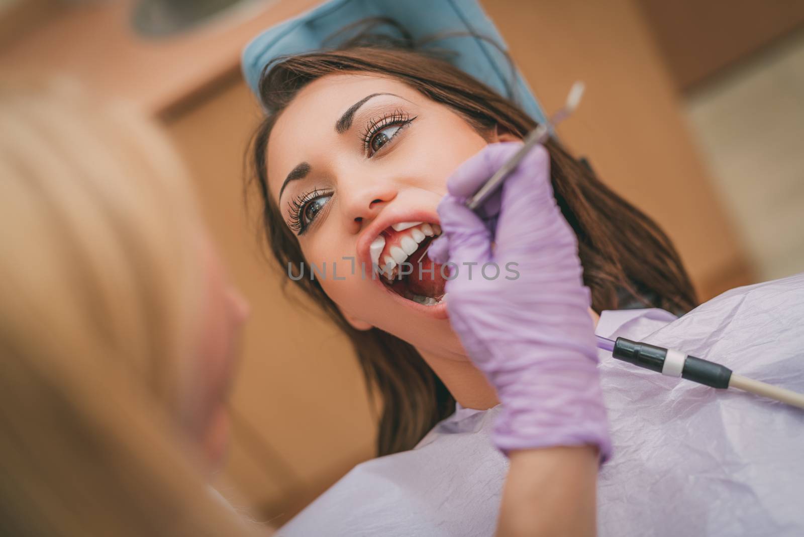 Beautiful young woman in visit at the dentist office. She is sitting on a chair and female dentist checkup teeth on her. Selective focus. Close-up.