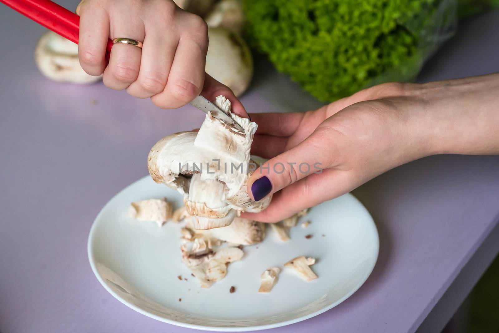 hands clean mushrooms with a knife over a white plate