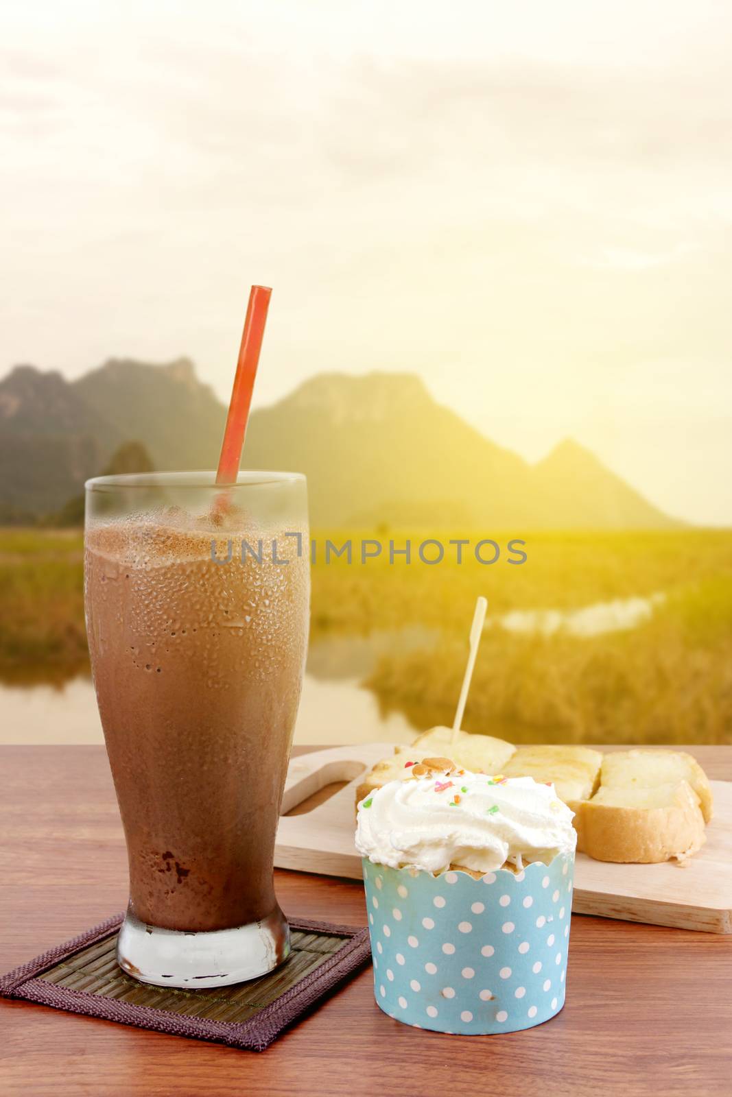 Cocoa chocolate smoothie in glass and Buttered bread and cup cake in morning. Warm lighting.