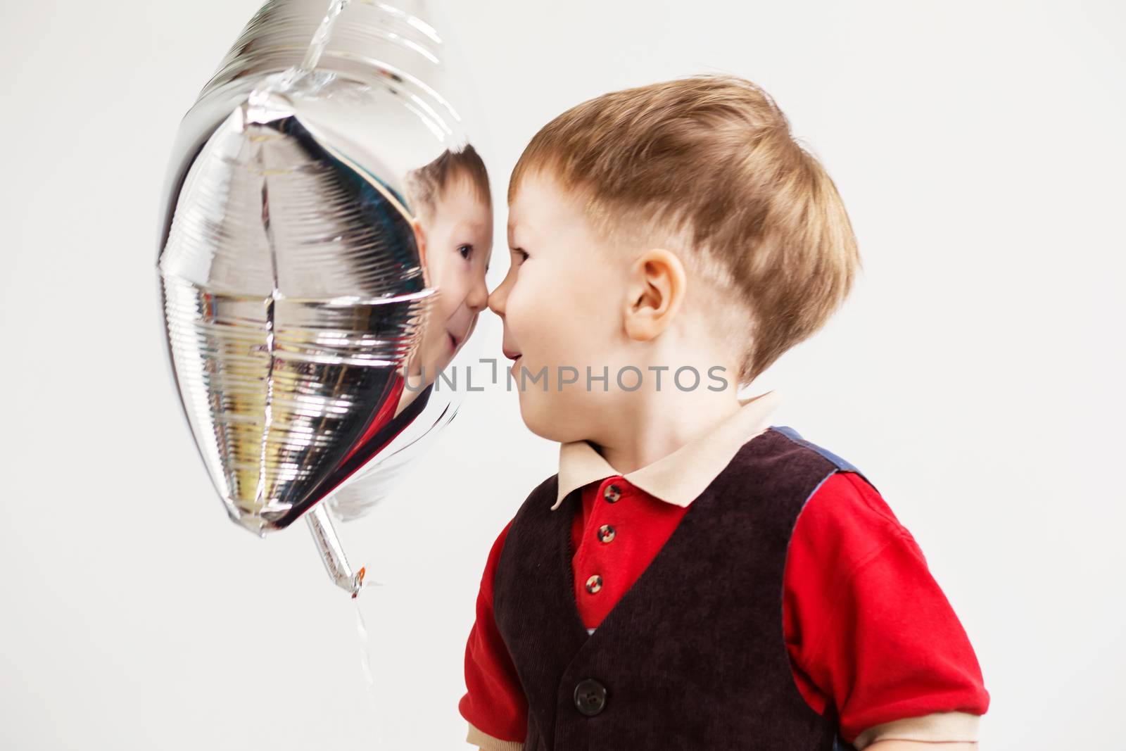 Boy grimacing and playing the ape with star-shaped balloons in studio. Kid looks and rejoices at his reflection in foil balloon. Child laughing looking at the reflection in a distorted mirror