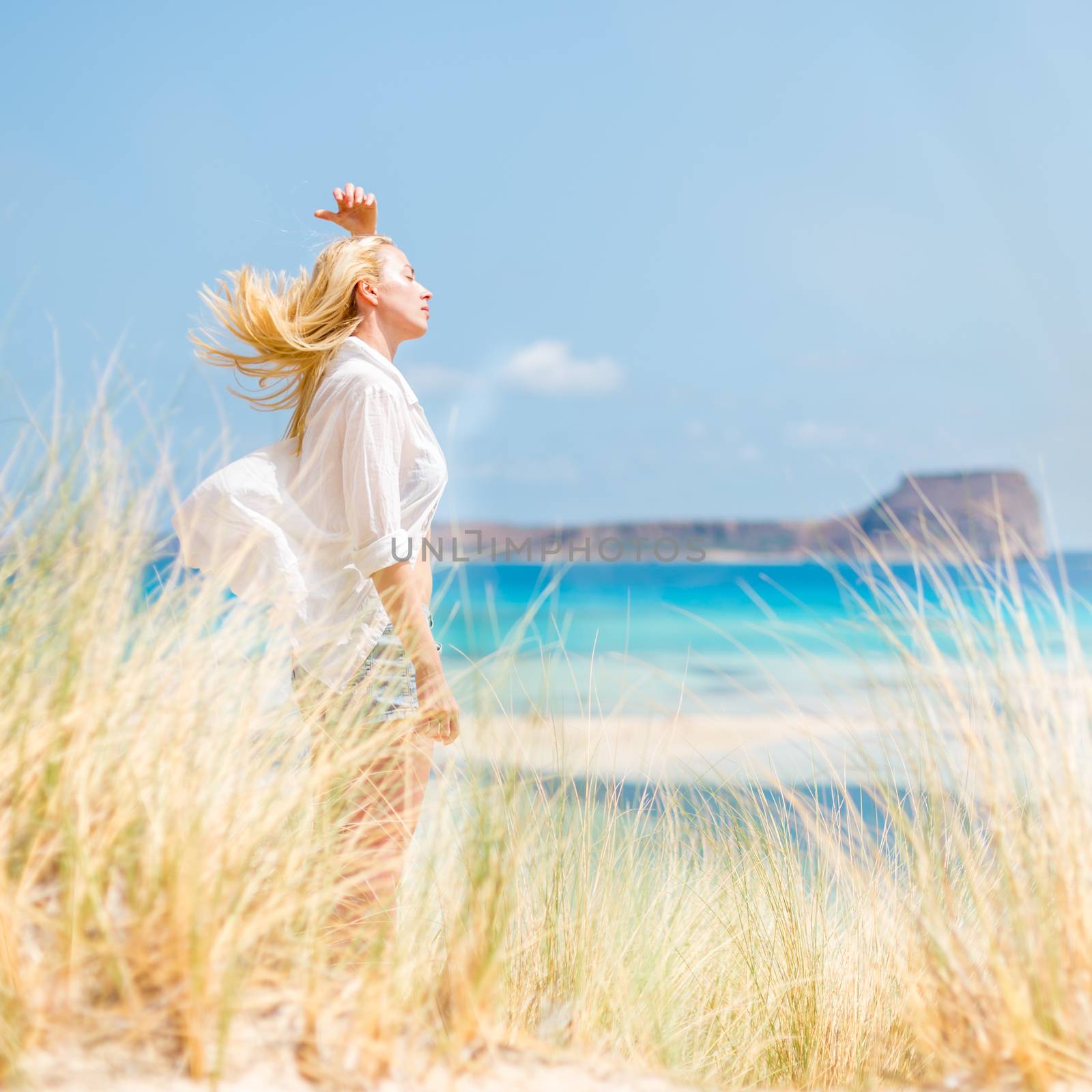 Relaxed woman enjoying sun, freedom and life an a beautiful beach. Young lady feeling free, relaxed and happy. Concept of vacations, freedom, happiness, enjoyment and well being.