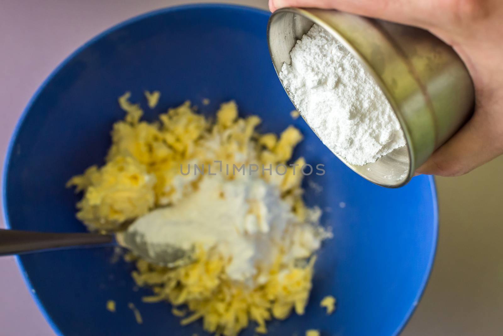 hand adds powdered sugar in butter over blue bowl