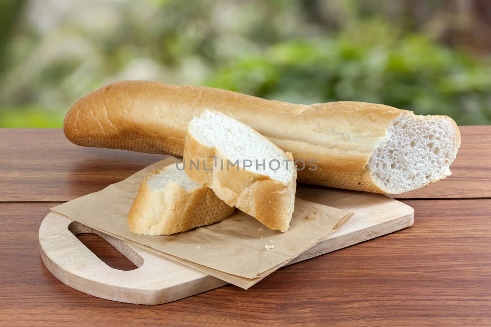 French bread baguette cut on brown paper with wooden board