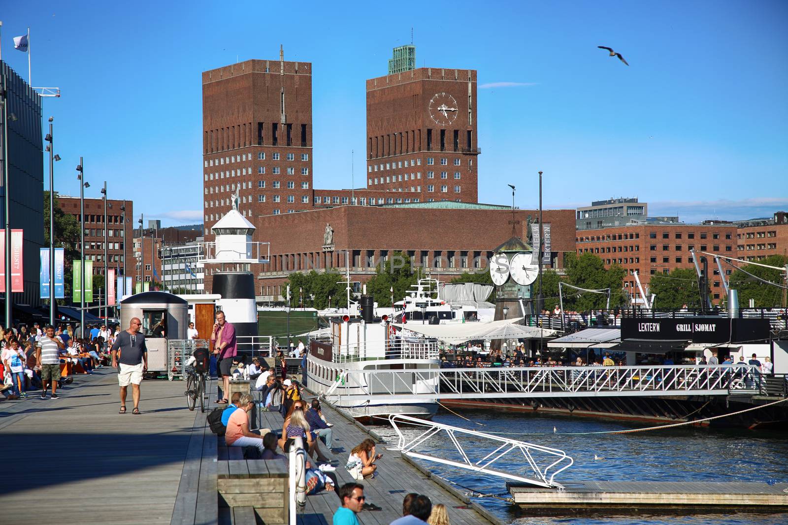 OSLO, NORWAY – AUGUST 17, 2016: People walking on modern district on street Stranden, Aker Brygge district and in the background is the City Hall in Oslo, Norway on August 17,2016.