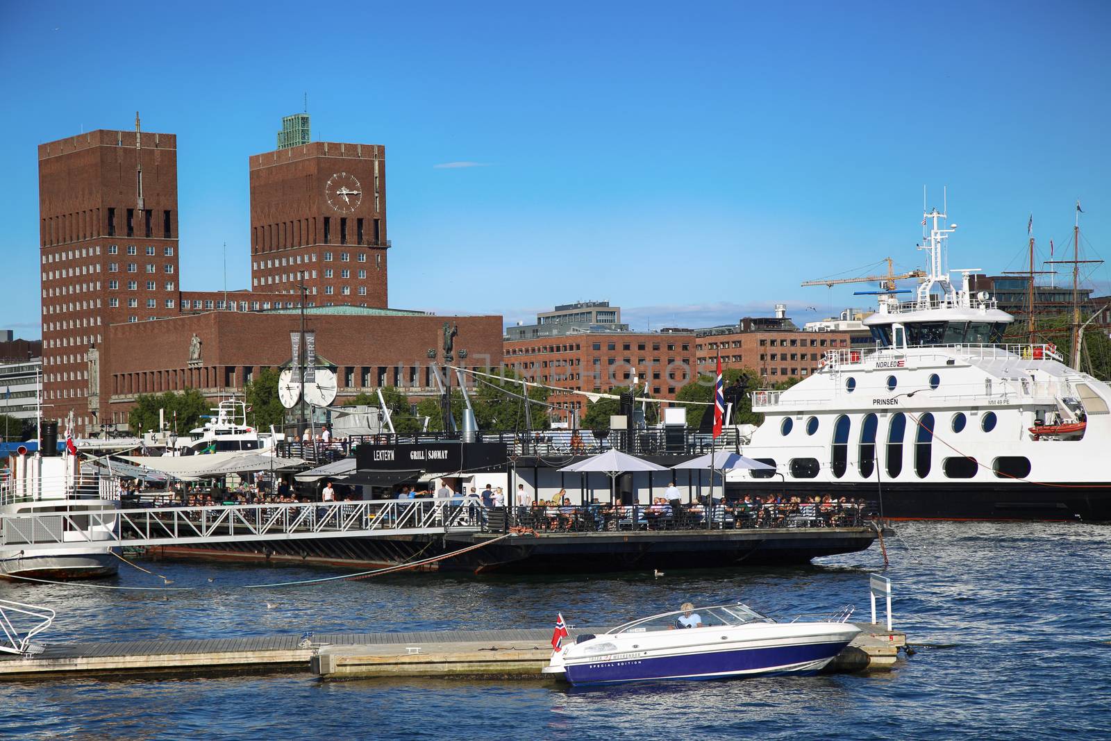 OSLO, NORWAY – AUGUST 17, 2016: People walking on modern district on street Stranden, Aker Brygge district and in the background is the City Hall in Oslo, Norway on August 17,2016.