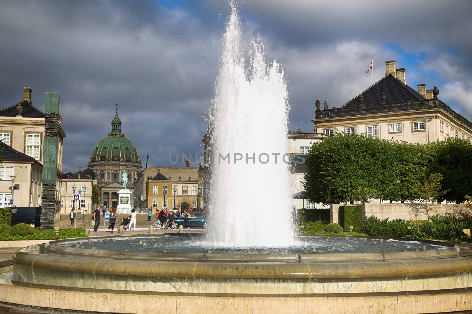 COPENHAGEN, DENMARK - AUGUST 15, 2016: A fountain in the Amalie Garden, with many tourist, in the background is Frederik's Church and Sculpture of Frederik V in Copenhagen, Denmark on August 15, 2016.