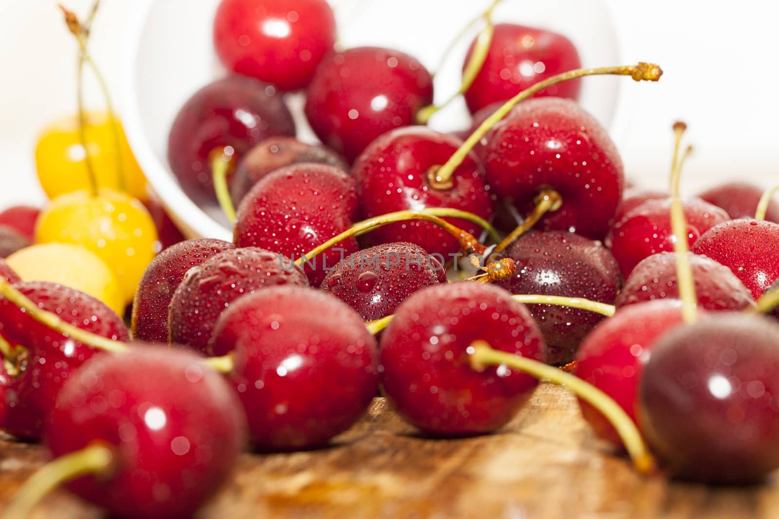 photographed close-up of ripe red cherries covered with water drops, shallow depth of field, white bowl on the table