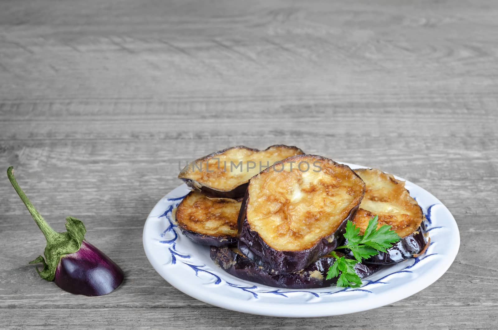 Fried eggplant on a white plate and grey wooden rustic background.