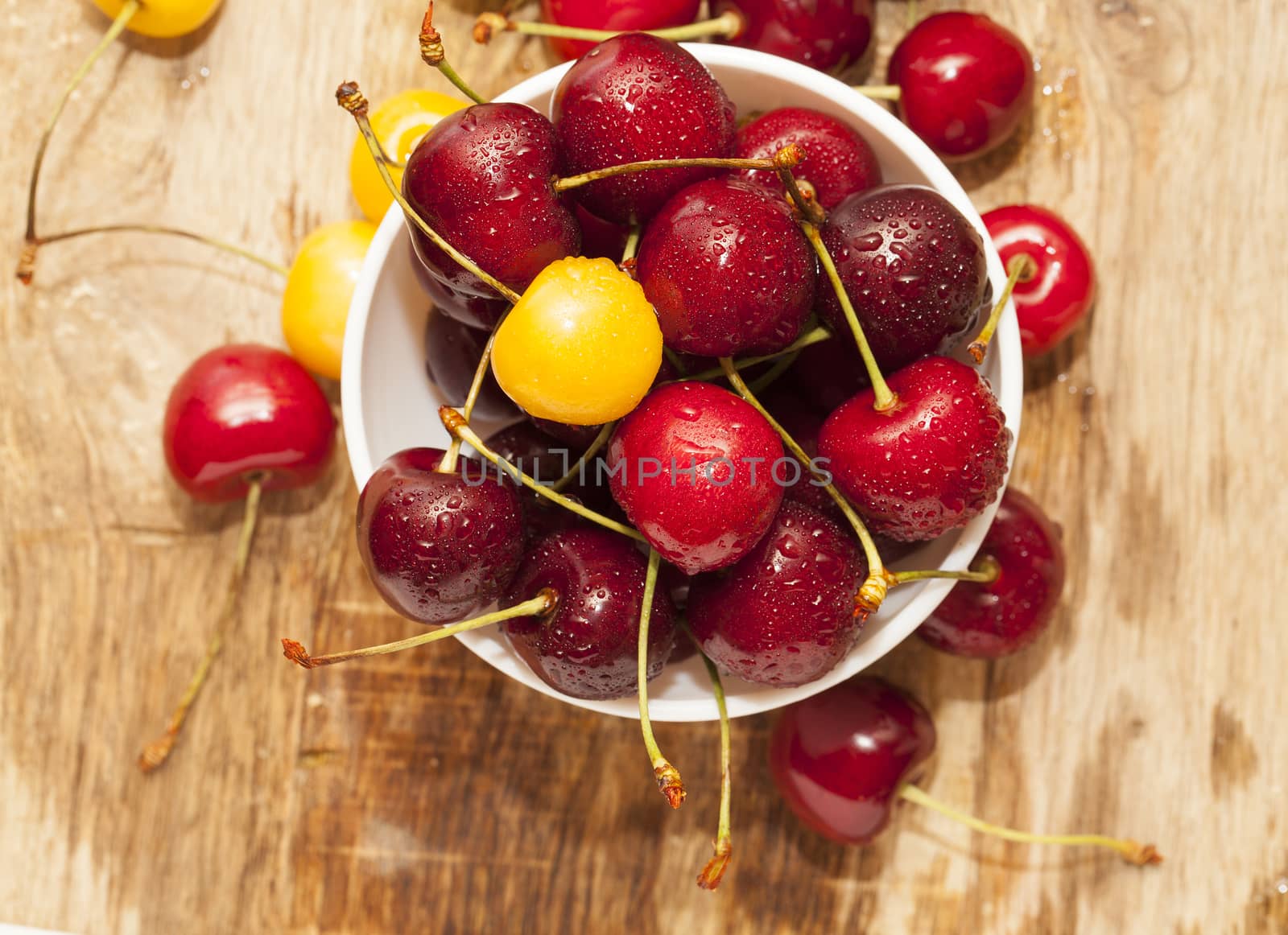 Photographed close-up ripe red cherries covered with drops of water, little depth of field, berries are on a wooden table in a white bowl