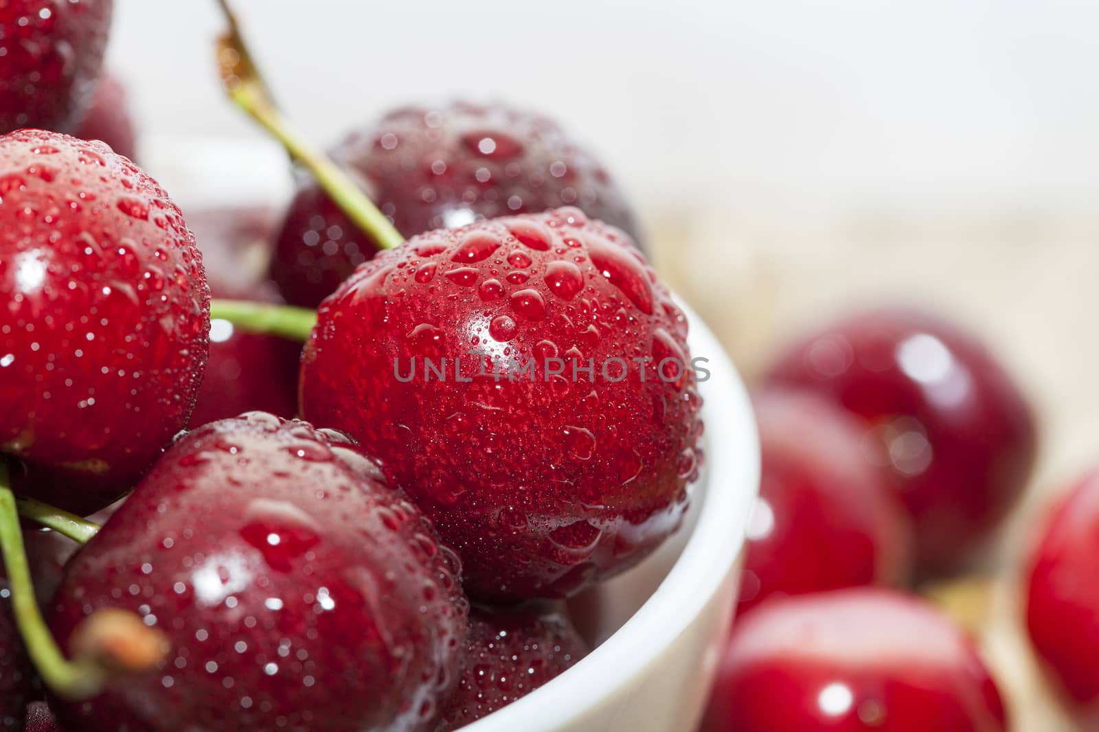 Photographed close-up ripe red cherries covered with drops of water, little depth of field, berries are on a wooden table in a white bowl