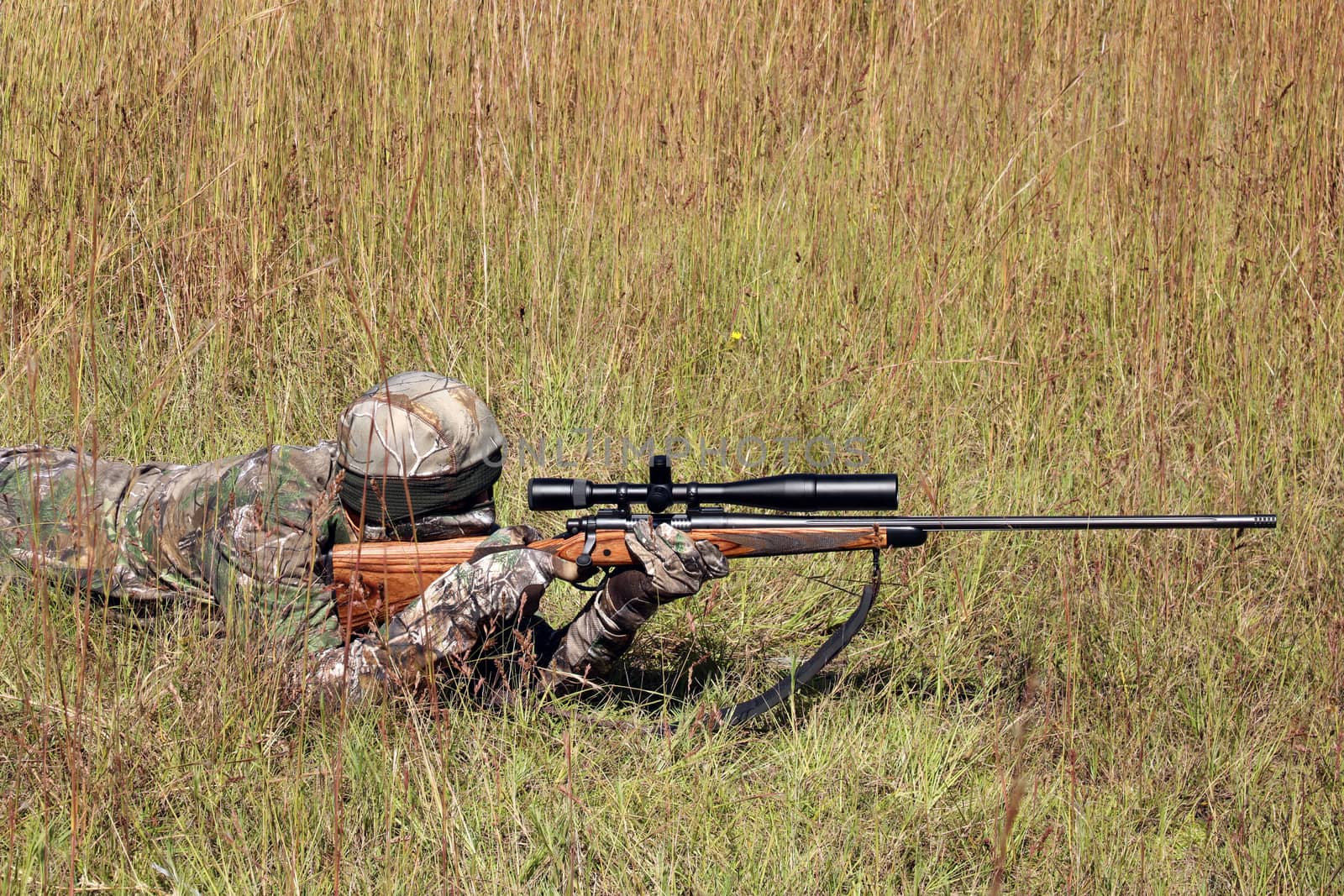 Hunter in grassy field with sniper rifle looking through scope at target