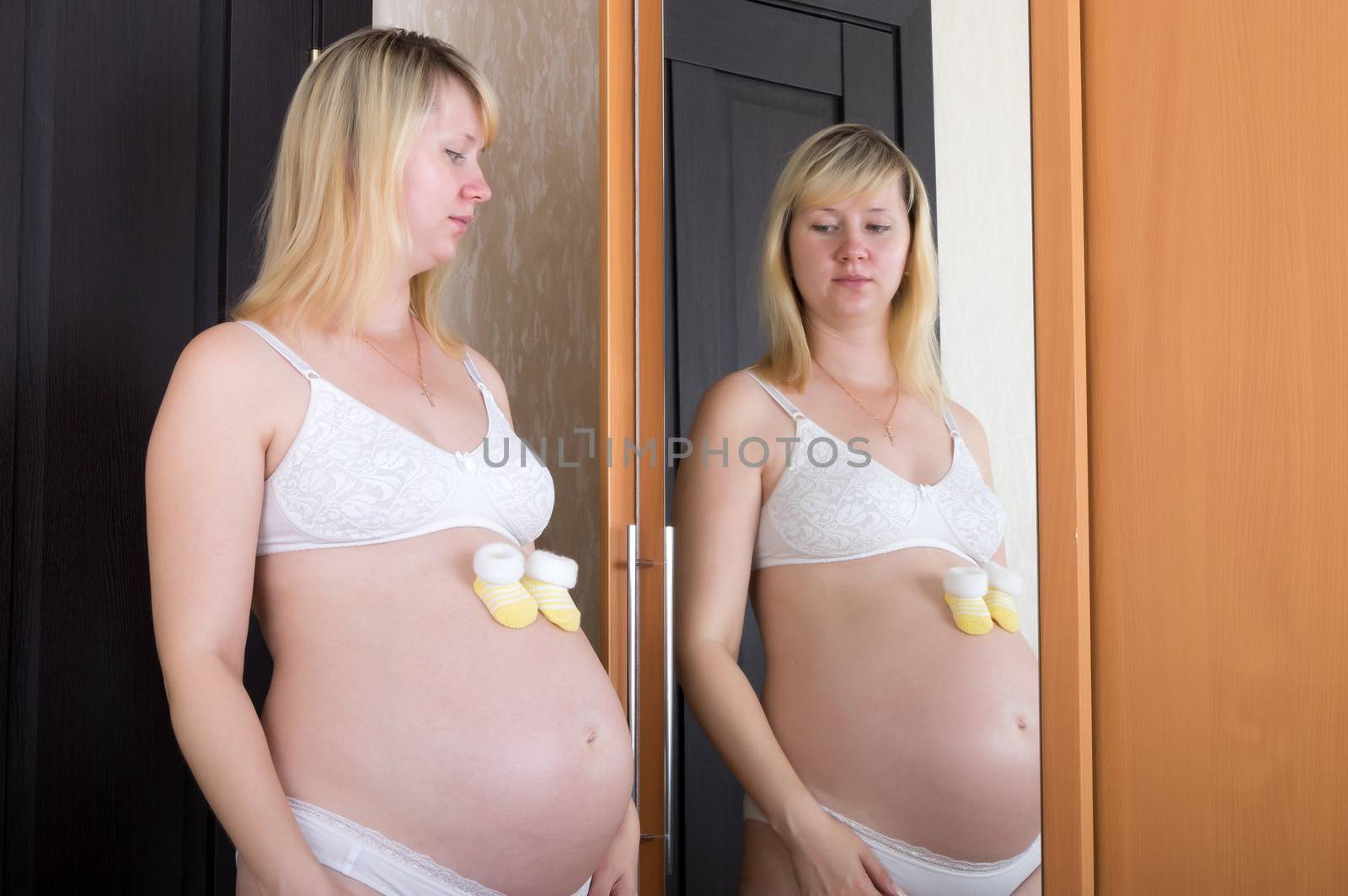Pregnant woman put booties on his stomach and looks in the mirror