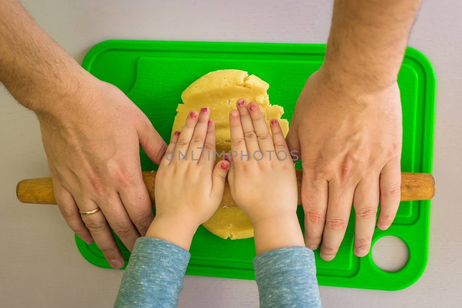 Children and dad hands rolled shortcrust dough with a rolling pin on the table