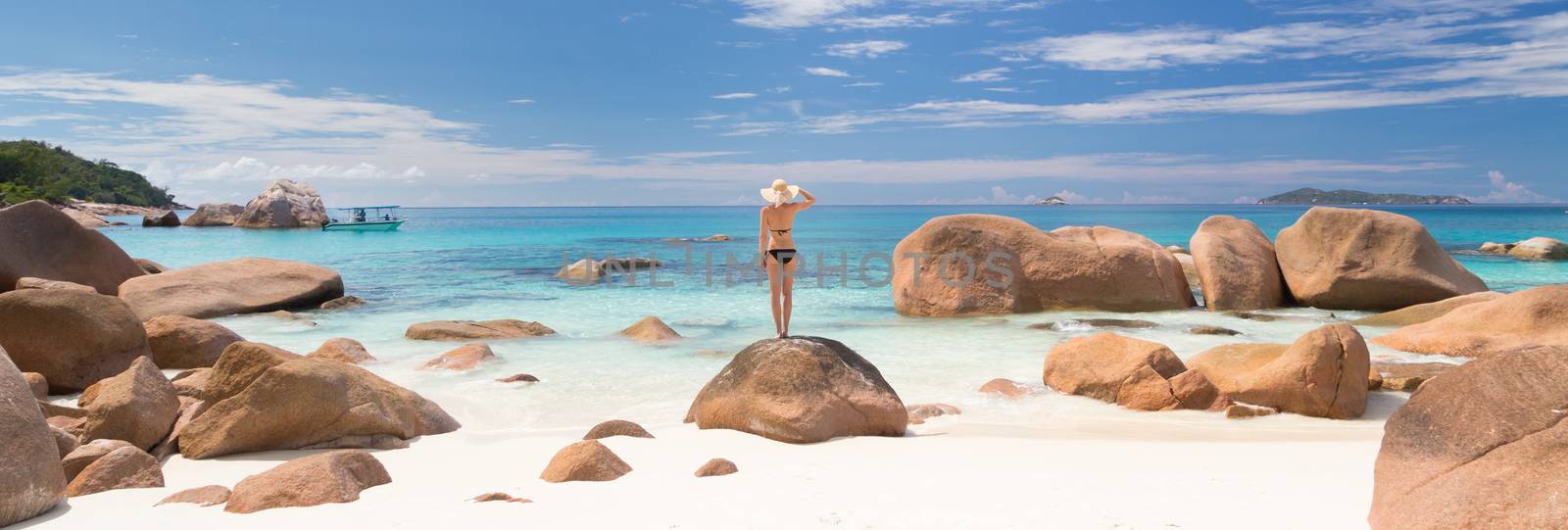 Woman wearing black bikini and beach hat, enjoying amazing view on Anse Lazio beach on Praslin Island, Seychelles. Summer vacations on picture perfect tropical beach concept.