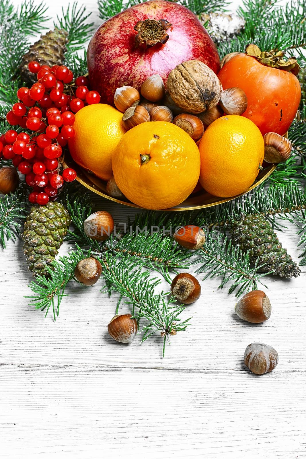 dish with tangerines,pomegranates,persimmons and nuts,decorated with fir branches
