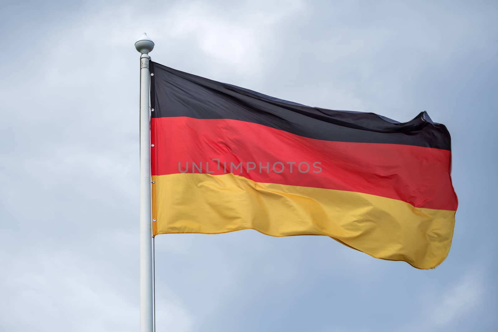 The flag of Germany flutters on wind against the background of gray clouds.