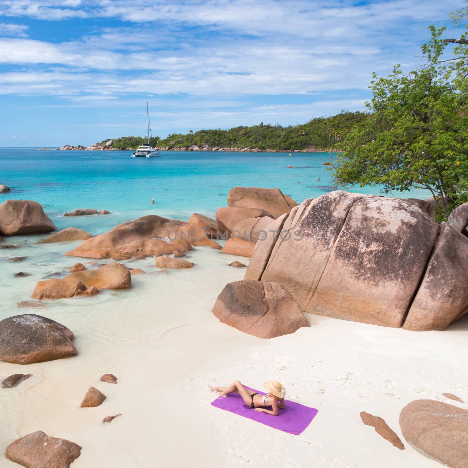 Woman wearing black bikini and beach hat, sunbathing at Anse Lazio beach on Praslin Island, Seychelles. Summer vacations on picture perfect tropical beach concept.