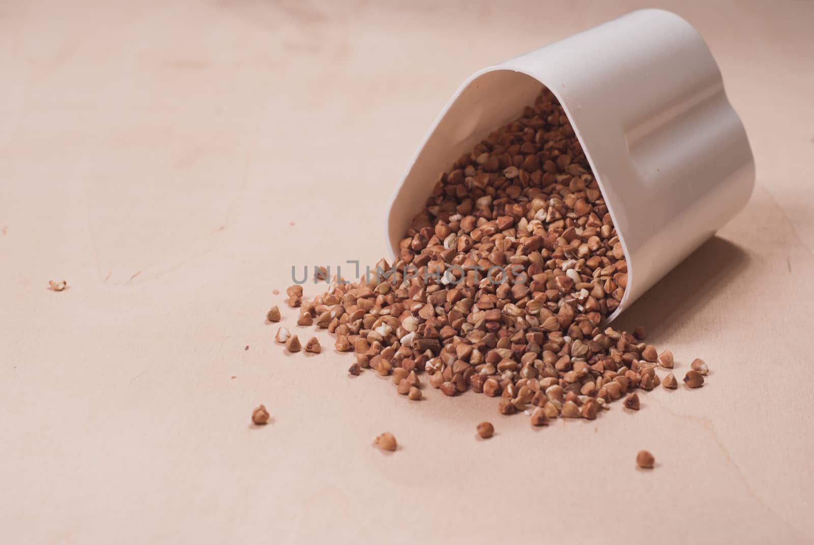 Buckwheat is scattered from the white container, wooden table, healthy food concept