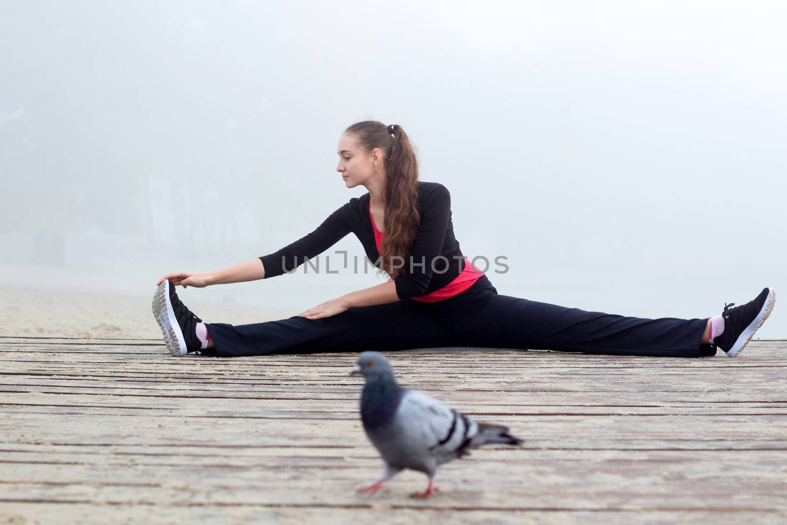 Young pretty slim fitness sporty woman does stretching exercises during training workout outdoor