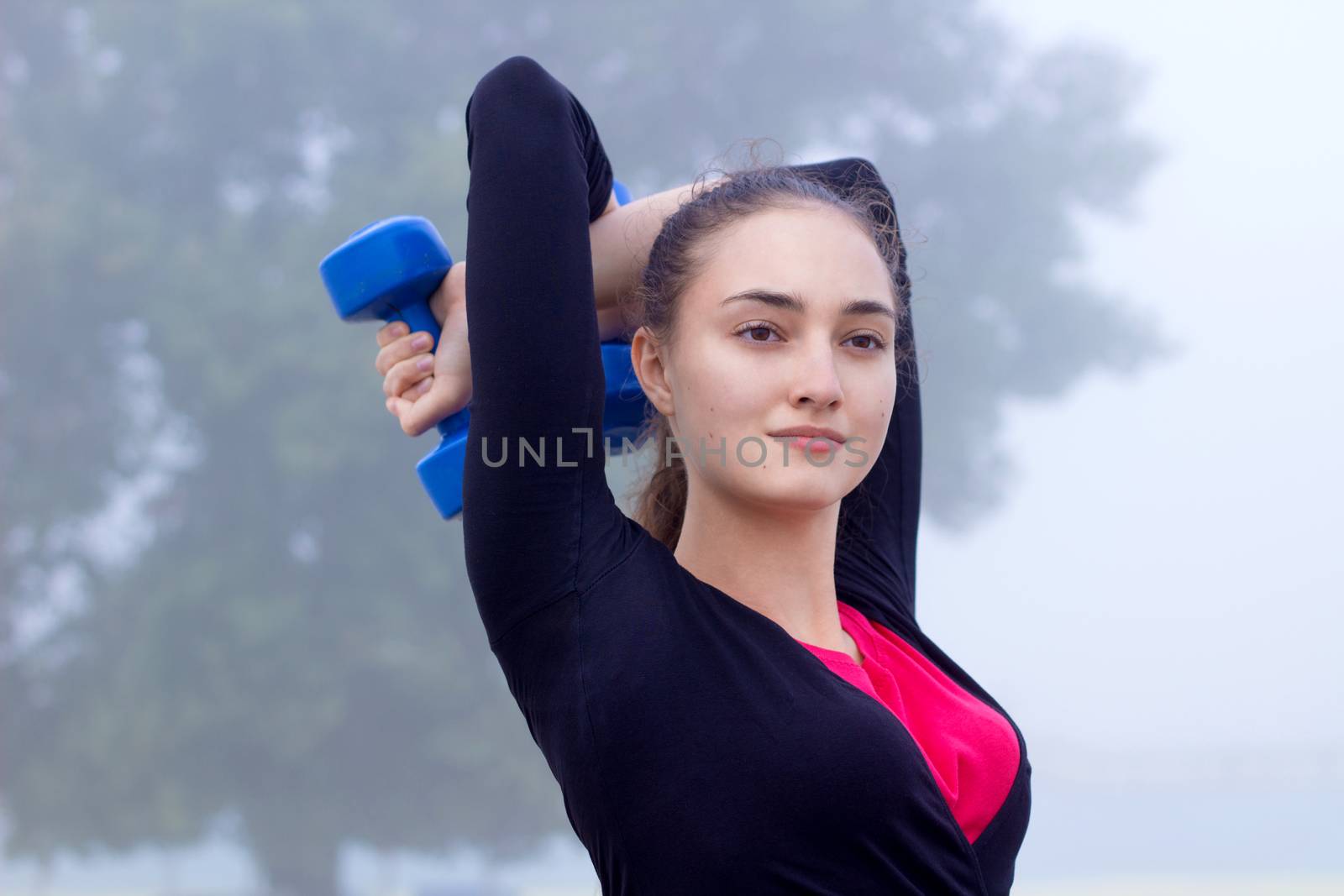 Young pretty slim fitness sporty woman exercises with weights dumbells during training workout outdoor