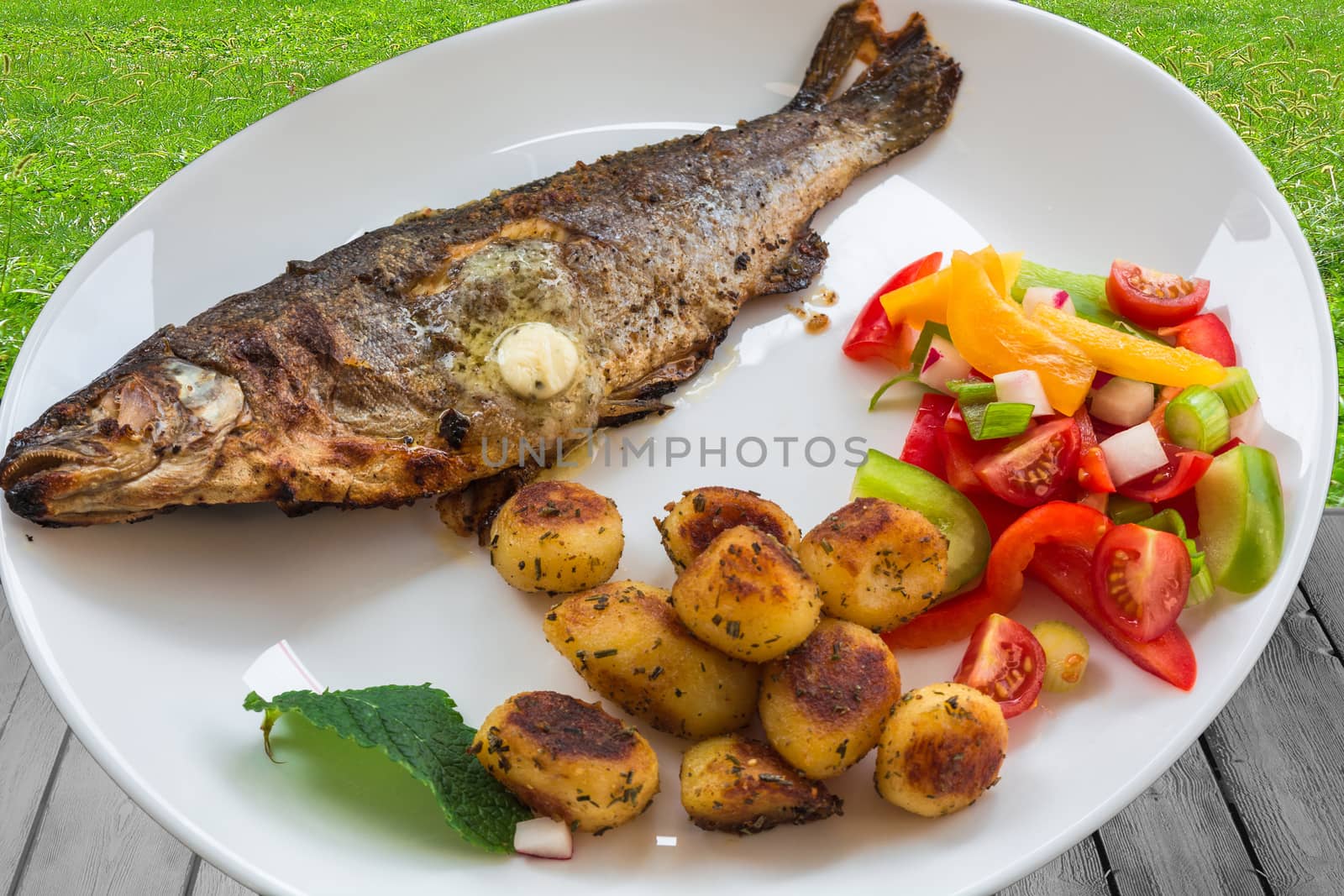 Roasted trout on white plate with lemon and roasted potatoes.