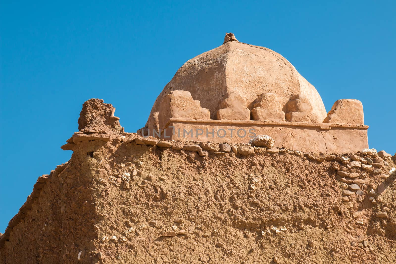 Old and not finished construction of a mosque on hill beside a road to the city Ait Ben Haddou. Dome without a tower. Bright blue sky.