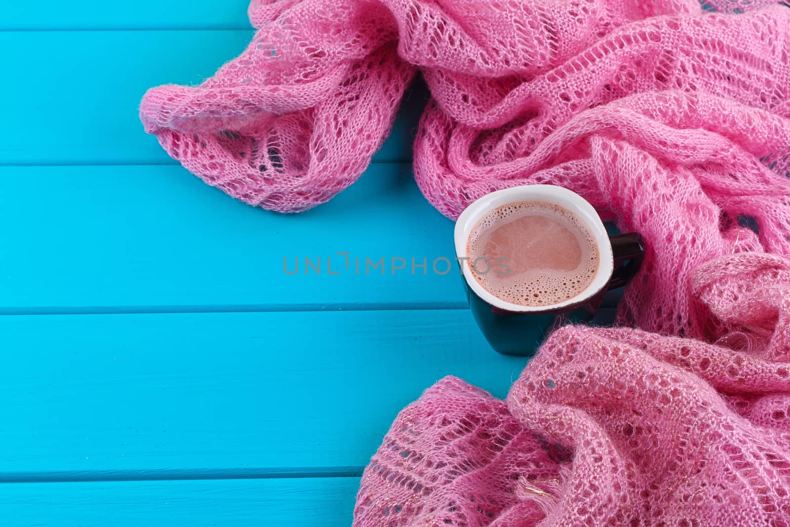 Cozy winter home background, cup of hot cocoa with marshmallow, old vintage books and warm knitted sweater on white painted wooden board background.