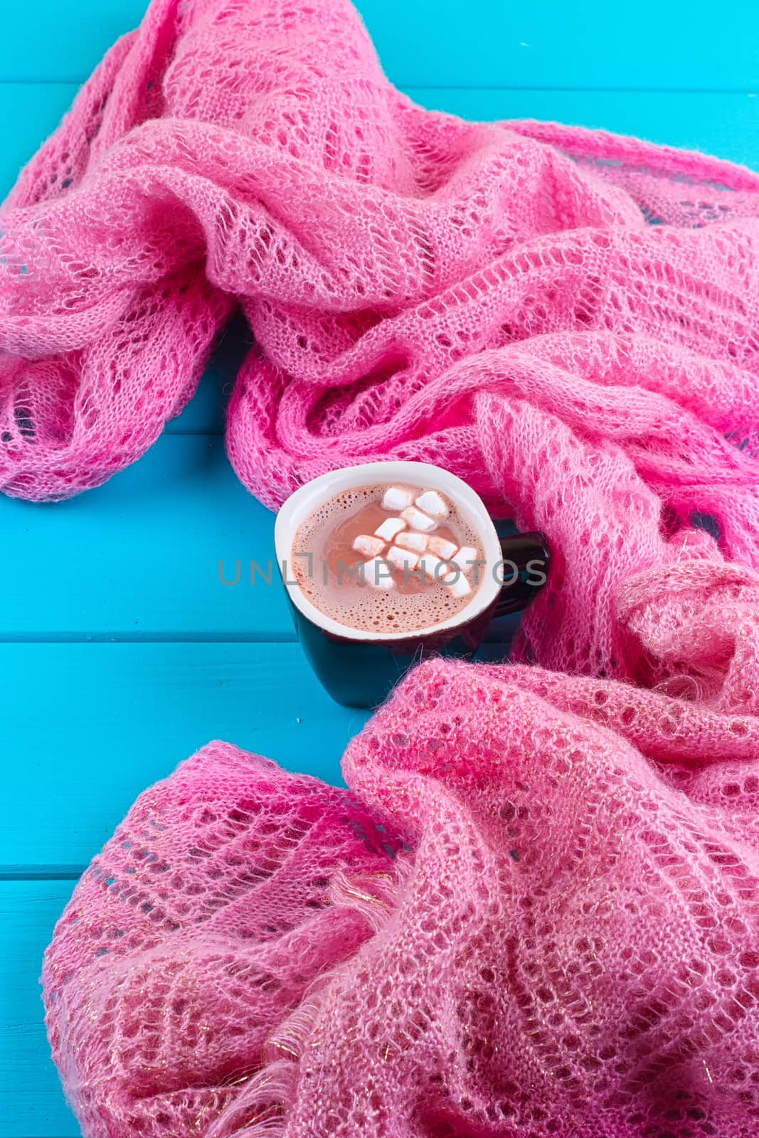 Cozy winter home background, cup of hot cocoa with marshmallow, old vintage books and warm knitted sweater on white painted wooden board background.