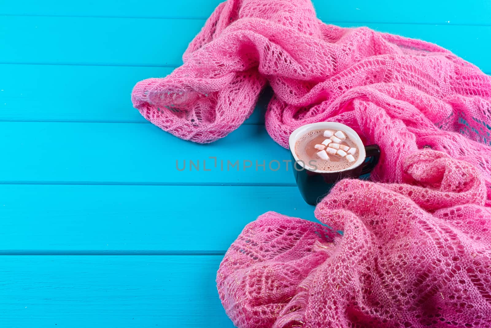 Cozy winter home background, cup of hot cocoa with marshmallow, old vintage books and warm knitted sweater on white painted wooden board background.