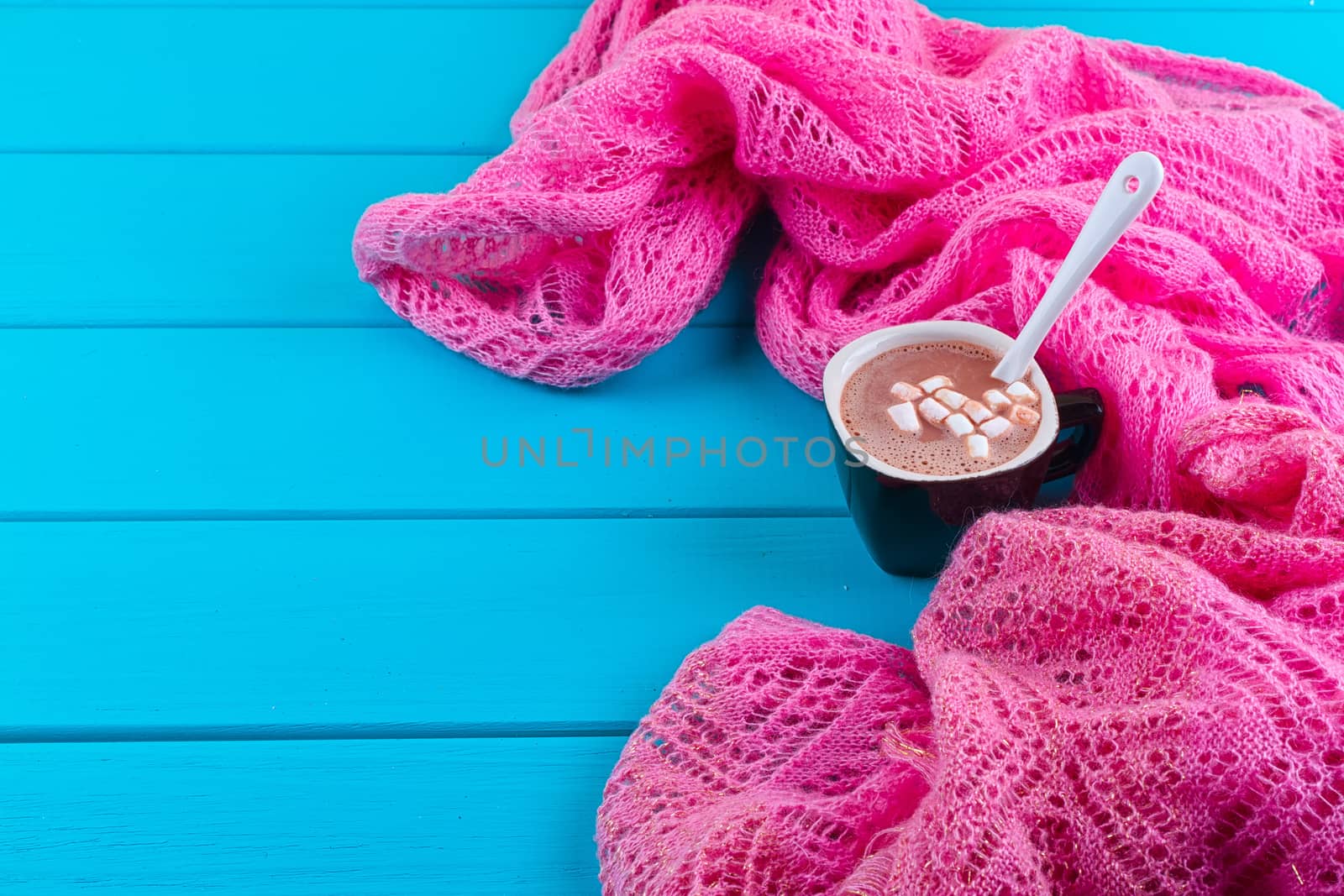 Cozy winter home background, cup of hot cocoa with marshmallow, old vintage books and warm knitted sweater on white painted wooden board background.