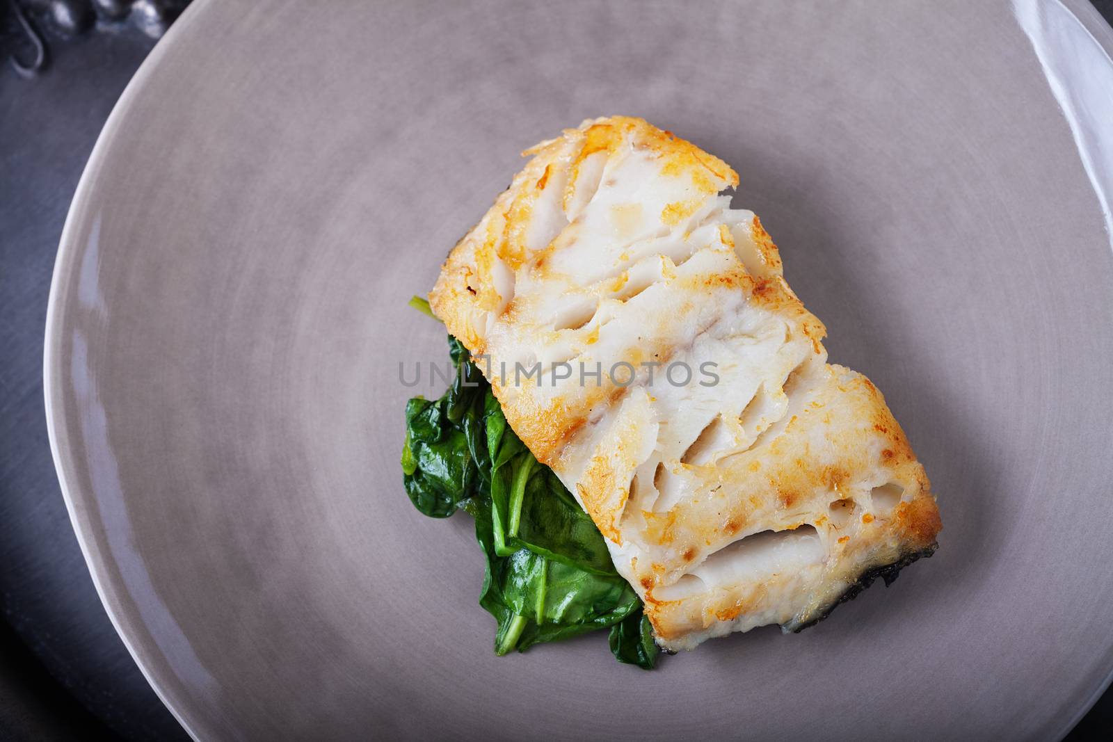 Fried cod fillets and spinach on a plate.