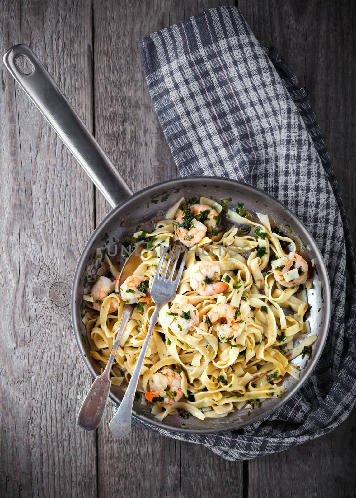 Tagliatelle with shrimps on the pan placed on a wooden table